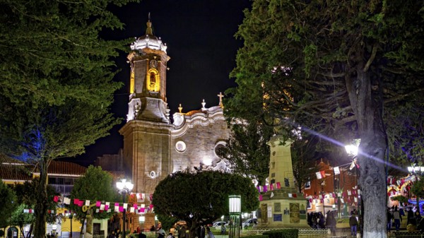 An illuminated church at night decorated with festive activities and flags, surrounded by trees, The churches of the city of Potosi in Bolivia