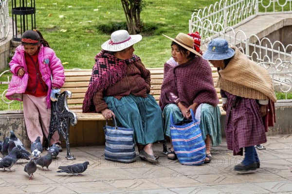Two woman, two children on a park bench talking while pigeons are nearby, woman and people in the streets of Potosi Bolivia