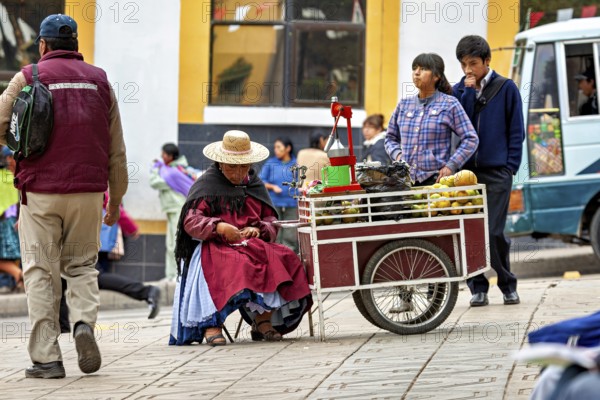 A saleswoman in a hat sits at a fruit stand on a busy pavement, selling fresh juice in the city of Potosi in Bolivia