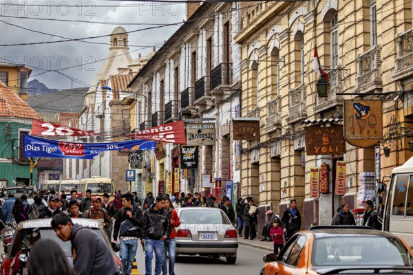 Busy street scene with colonial architecture. People and cars animate the street under a slightly cloudy sky, people in the streets of Potosi in Bolivia