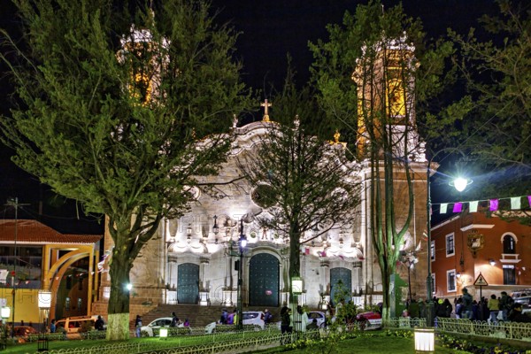 Illuminated church at night surrounded by trees and celebrating people, The churches of the city of Potosi in Bolivia