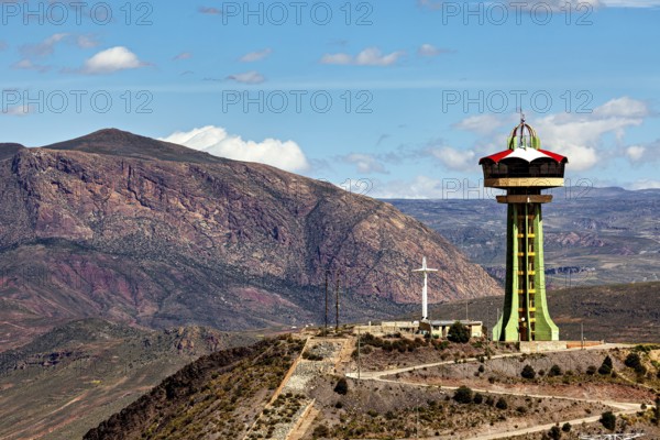 Observation tower next to cross and rocky mountain under blue sky with clouds, The water tower of the city of Potosi in Bolivia