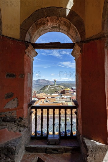 View through an old stone and wooden window of the city and mountains in sunny weather, view of the water tower of the city of Potosi in Bolivia
