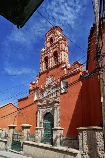 Colonial building with red façade and bell tower, surrounded by power lines and a clear sky, The churches of the city of Potosi in Bolivia