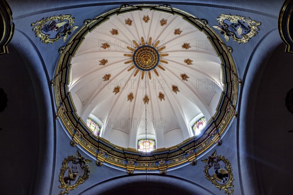 Dome of a church with golden decorations on a blue background and light through windows, inside the cathedral of Potosi in Bolivia