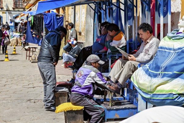Lively street scene with people at a South American market, a shoeshine boy at work, shoeshine boy in the streets of Potosi in Bolivia