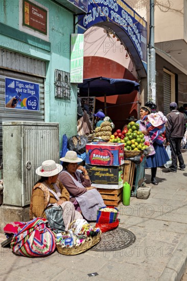 Women in traditional dress sell fruit at a busy market stall in a Bolivian town, selling goods in the market halls of Potosi in Bolivia