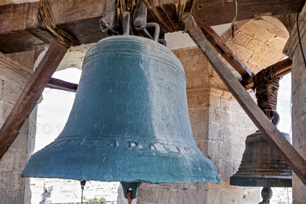 Two large bells hang in a historic bell tower with stone pillars and wooden beams, The large bell of Potosi Cathedral in Bolivia