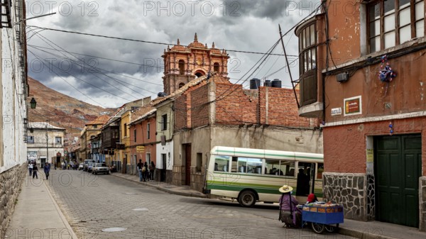 A lively street with colourful buildings against a backdrop of mountains and a bus. The atmosphere is traditional and lively, The streets in the historic centre of Potosi in Bolivia