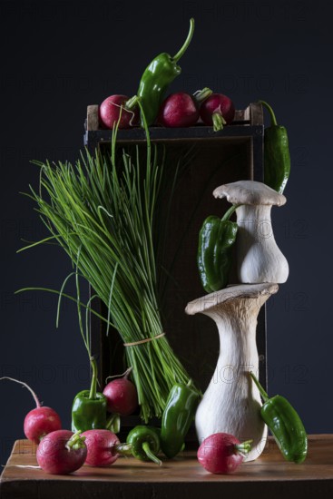 oyster mushrooms with radishes, chives and chillies on a wooden crate against a dark background