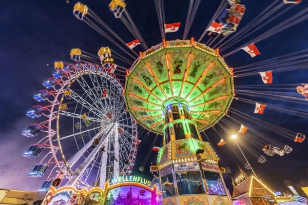 Folk festival time in Stuttgart. Ferris wheel and chain carousel in the evening. The 178th Cannstatter Volksfest on the Wasen is one of the most important traditional festivals in Germany. In addition to the large festival tents, the Wasen is characterised by fairground attractions. Around 320 showmen, festival hosts and market traders expect around four million visitors. Bad Cannstatt, Stuttgart, Baden-Württemberg, Germany