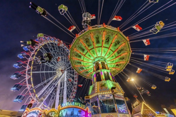 Folk festival time in Stuttgart. Ferris wheel and chain carousel in the evening. The 178th Cannstatter Volksfest on the Wasen is one of the most important traditional festivals in Germany. In addition to the large festival tents, the Wasen is characterised by fairground attractions. Around 320 showmen, festival hosts and market traders expect around four million visitors. Bad Cannstatt, Stuttgart, Baden-Württemberg, Germany