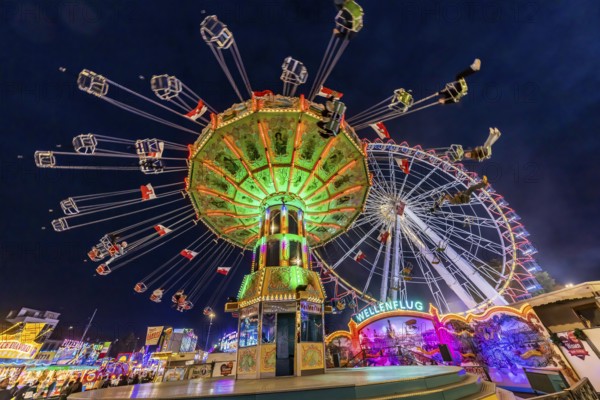 Folk festival time in Stuttgart. Ferris wheel and chain carousel in the evening. The 178th Cannstatter Volksfest on the Wasen is one of the most important traditional festivals in Germany. In addition to the large festival tents, the Wasen is characterised by fairground attractions. Around 320 showmen, festival hosts and market traders expect around four million visitors. Bad Cannstatt, Stuttgart, Baden-Württemberg, Germany