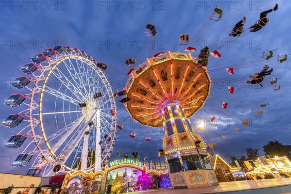 Folk festival time in Stuttgart. Ferris wheel and chain carousel in the evening. The 178th Cannstatter Volksfest on the Wasen is one of the most important traditional festivals in Germany. In addition to the large festival tents, the Wasen is characterised by fairground attractions. Around 320 showmen, festival hosts and market traders expect around four million visitors. Bad Cannstatt, Stuttgart, Baden-Württemberg, Germany