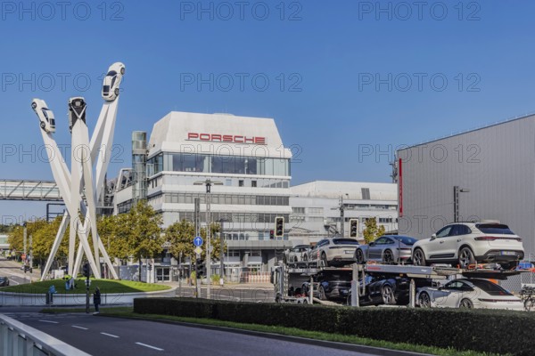 Porscheplatz with Porsche headquarters. Inspiration 911 artwork by Gerry Judah: three steles, each up to 24 metres high, presenting a Porsche 911. Car transporter with new cars. Stuttgart, Baden-Württemberg, Germany