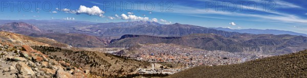 Panoramic view over a city in a wide valley with surrounding mountains under a cloudy sky, view over the city of Potosi in Bolivia