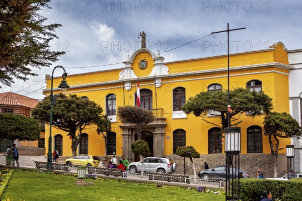 Yellow building with flags in an urban environment, surrounded by cars and green areas, house facade in the city of Potosi Bolivia