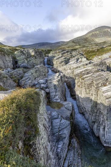 Deep gorge with meandering watercourse, surrounded by jagged rocks and mountains under a cloudy sky, Peer Gynt hytta, Rondane National Park, Otta, Innlandet, Norway