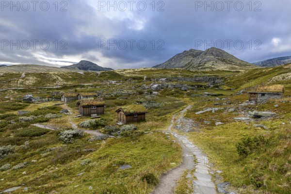 Wooden huts in an open meadow in a remote mountain landscape, with winding paths and clouds in the sky, Peer Gynt hytta, Rondane National Park, Otta, Innlandet, Norway