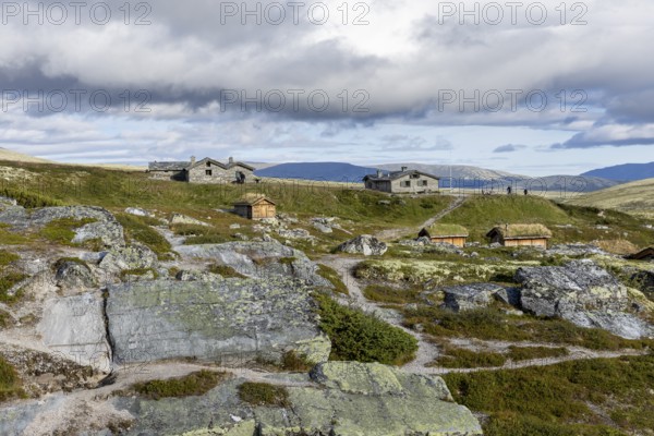 Various wooden cabins on a rocky plain, surrounded by grass and mountains under a cloudy atmosphere, Peer Gynt hytta, Rondane National Park, Otta, Innlandet, Norway
