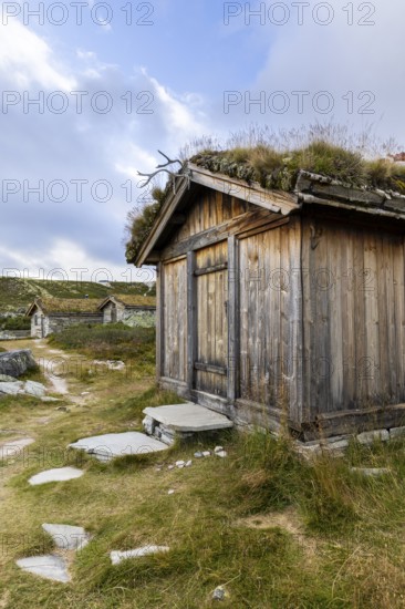 Wooden hut with grass roof and path in a rural setting under a blue sky with clouds, Peer Gynt hytta, Rondane National Park, Otta, Innlandet, Norway