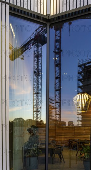 The picture shows the interior of a modern Berlin pub, taken in the evening. The scene is characterised by modern lighting fixtures reminiscent of large, glowing light bulbs. Scaffolding can be seen through the glass window, Berlin, Germany
