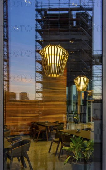 The picture shows the interior of a modern Berlin pub, taken in the evening. The scene is characterised by modern lighting fixtures reminiscent of large, glowing light bulbs. Scaffolding can be seen through the glass window, Berlin, Germany