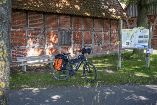 Bicycle in front of an old brick wall, next to it an information board in the sunshine, Weser cycle path, Scheunenviertel Schlüsselburg, Petershagen, North Rhine-Westphalia