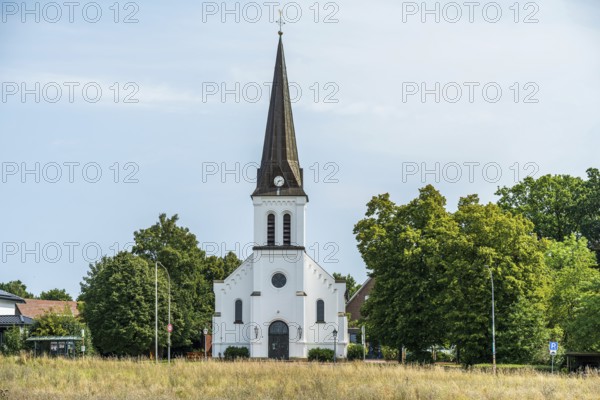 White church with tower and clock, embedded in a green landscape under a blue sky, Herford, Westphalia, North Rhine-Westphalia