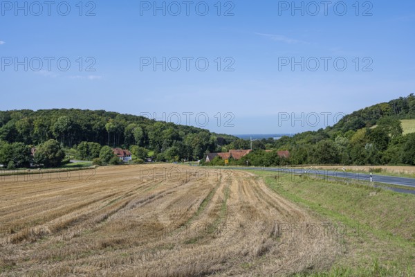 View of a harvested field with neighbouring village and wooded hills under a clear sky, Halle, Westphalia
