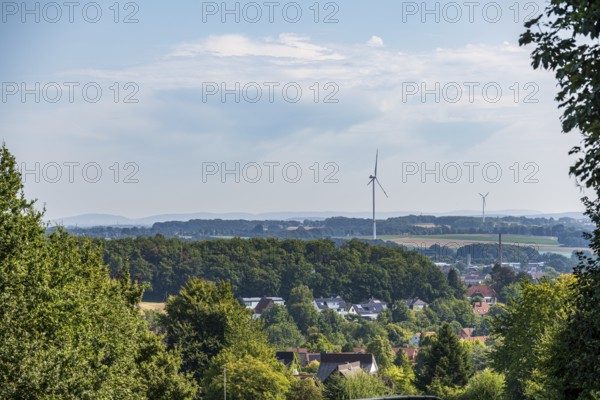 Landscape view with wind turbines and a village surrounded by green forests under a slightly cloudy sky, Halle, Werther, Westphalia