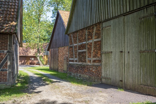 Path leads between rustic half-timbered houses made of brick and wood, surrounded by trees, Weser cycle path, Schlüsselburg barn quarter, Petershagen, North Rhine-Westphalia