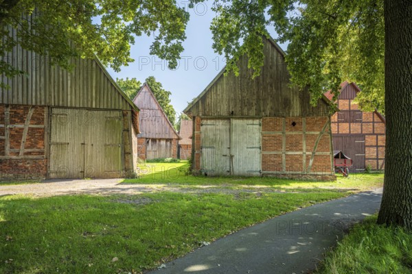 Rural path leads between old half-timbered houses surrounded by trees, Weser cycle path, Schlüsselburg barn quarter, Petershagen, North Rhine-Westphalia
