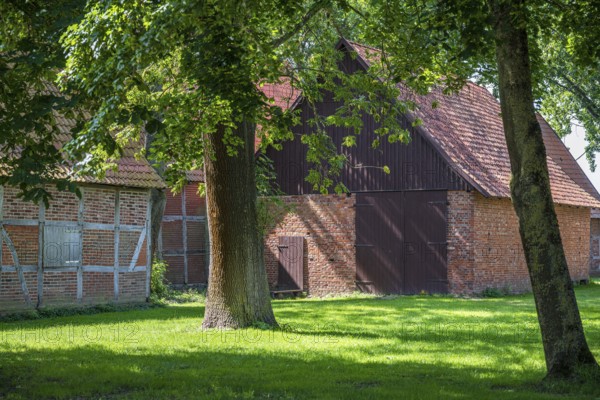 Large brick and wooden barn surrounded by trees and green grass, Weser cycle path, Schlüsselburg barn quarter, Petershagen, North Rhine-Westphalia
