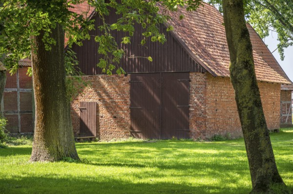 Old brick and timber barn surrounded by trees in rural area, Weser cycle path, Schlüsselburg barn quarter, Petershagen, North Rhine-Westphalia
