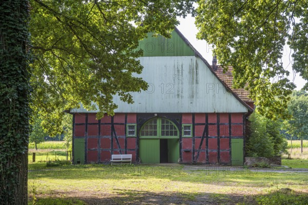 A traditional red and green half-timbered barn surrounded by trees on a sunny day, Gütersloh, Westphalia