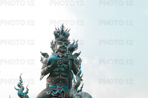 A statue of a mythical figure with intricate details against a pale sky in Wat Rong Suea Ten or Blue Temple. Chiang rai, Thailand