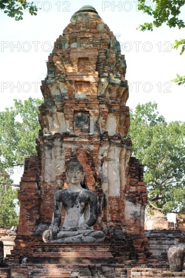 A Buddha statue seated before an ancient brick stupa, surrounded by greenery, exuding serenity in Wat Chaiwatthanaram in Ayutthaya, Thailand