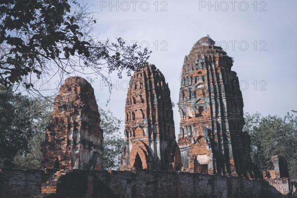 Tall brick ruins and towers reaching towards the sky amidst surrounding trees, evoking antiquity. Wat Chaiwatthanaram in Ayutthaya, Thailand