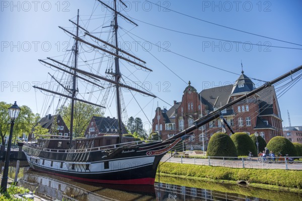 A historic sailing ship on a sunny day with a striking brick building in the background, The sailing ship Frederike von Papenburg in front of the town hall in Papenburg