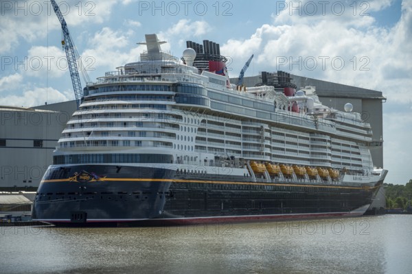 A large cruise ship lies calmly in the water next to a large shipyard on a partly cloudy day, cruise ship in the Meyer shipyard in Papenburg