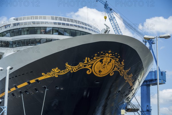 A detailed decorated bow of a cruise ship under a cloudy sky with a crane in the background, cruise ship in the Meyer shipyard of Papenburg