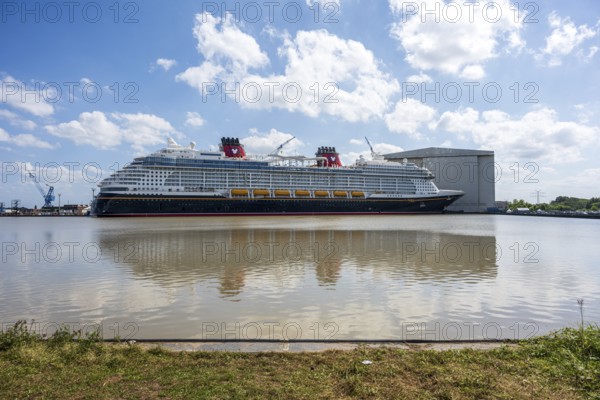 A cruise ship lies in the water, surrounded by a shipyard and a grassy embankment, cruise ship in the Meyer shipyard in Papenburg