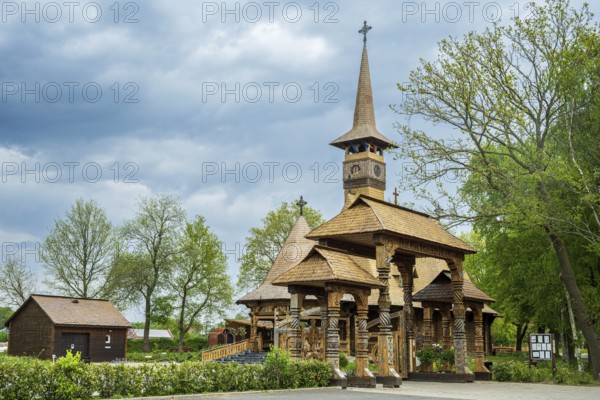 Impressive wooden church with elaborate wood carvings, surrounded by trees under a cloudy sky, The Romanian Orthodox church near Sögel in Emsland
