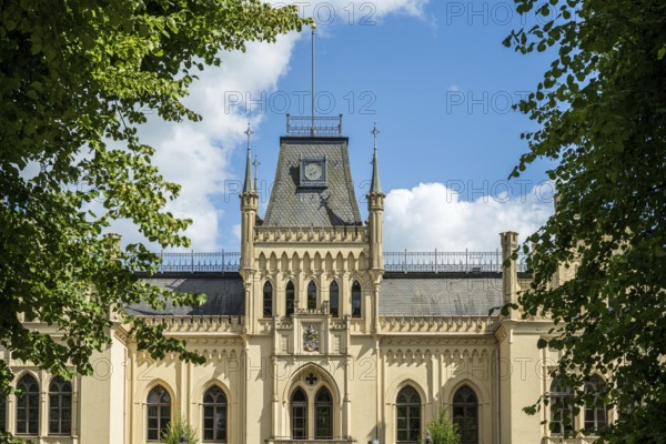 A Gothic castle with towers surrounded by green trees under a blue sky, Schloss Evenburg, Leer, East Frisia