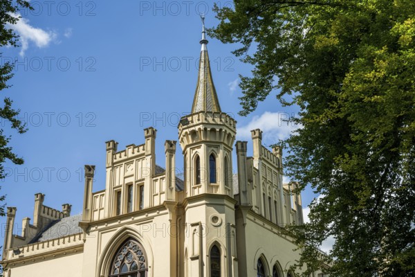 The Gothic-style castle tower rises into the blue sky, surrounded by trees, Schloss Evenburg, Leer, East Frisia