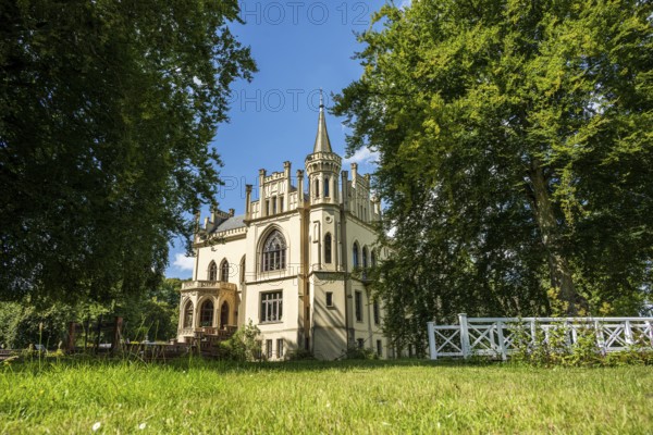 Historic castle with Gothic elements, surrounded by meadow and trees under a blue sky, Schloss Evenburg, Leer, East Frisia