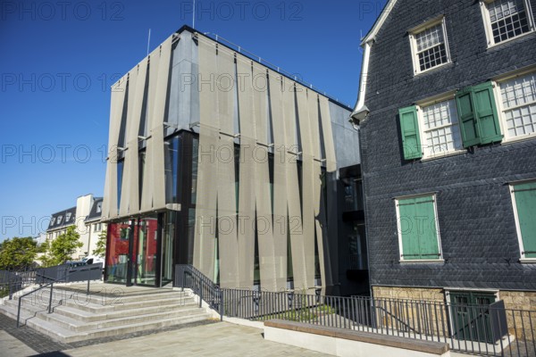 Modern building with a striking façade and large glass windows next to a traditional house under a blue sky, Museum of Early Industrialisation in Wuppertal Barmen