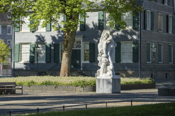 Stone figure in front of a historic building with green shutters, surrounded by blossoming trees, statue The Strong Left by Alfred Hrdlicka in front of the Friedrich Engels House in Wuppertal Barmen