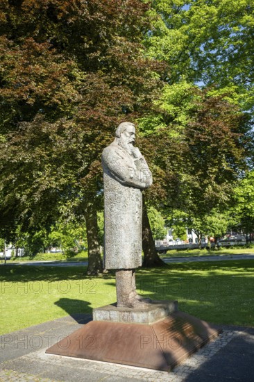 Side view of a stone statue of a pensive man in a green park with trees, statue of Friedrich Engels by sculptor Zeng Chenggang in the Engelsgarten Wuppertal Barmen